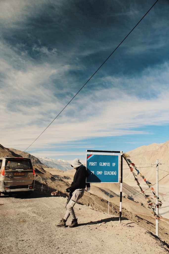 A guy standing on the highway doing hitchhiking.